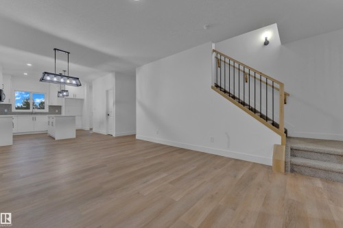 Open-concept living area featuring wood-finish flooring, a modern kitchen with white cabinetry, a kitchen island, and contemporary light fixtures - 4213 63 Street, Beaumont, AB 