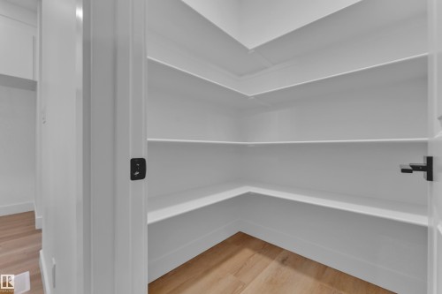 Walk-in pantry featuring white shelving, light wood-finish flooring, and matte black door hardware - 4213 63 Street, Beaumont, AB 