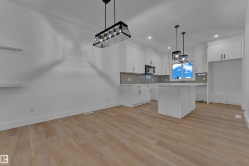 Open-concept kitchen and dining area featuring light wood-finish flooring, white cabinetry, a central island, and modern pendant lighting fixtures - 4213 63 Street, Beaumont, AB 