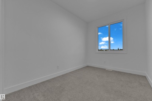 Bright room featuring a large window, neutral gray carpeting, white walls, and clean baseboards - 4213 63 Street, Beaumont, AB 