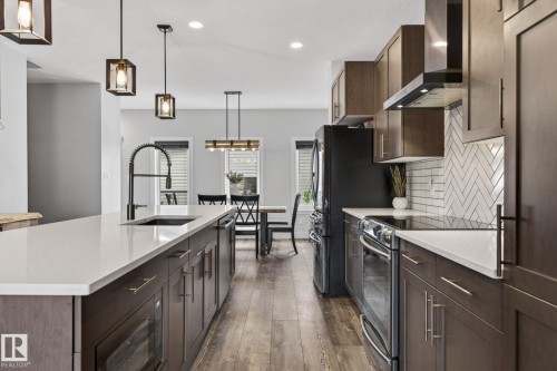 Modern kitchen featuring an expansive center island with an undermount sink and matte black faucet, wood-finish flooring, white countertops, and a white subway tile backsplash with a herringbone pattern - 17733 64A Street, Edmonton, AB 