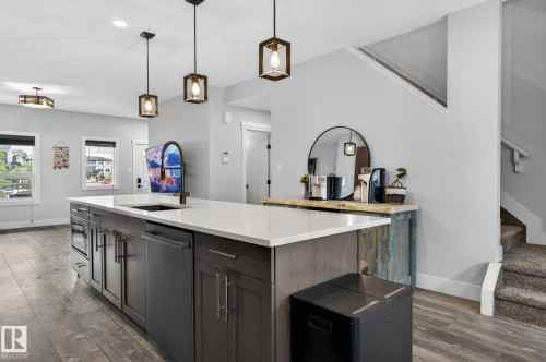 Central kitchen island featuring a white countertop, an undermount sink with a black arched faucet, integrated dishwasher, and dark wood-finish cabinetry - 17733 64A Street, Edmonton, AB 