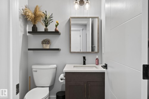Bathroom featuring a dark wood-finish vanity with a light countertop, a rectangular sink with a matte black faucet, and a wall-mounted mirror with a wood-finish frame - 17733 64A Street, Edmonton, AB 