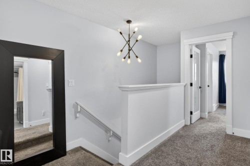Upper-level landing featuring neutral carpeting, a contemporary chandelier, and white trim - 17733 64A Street, Edmonton, AB 