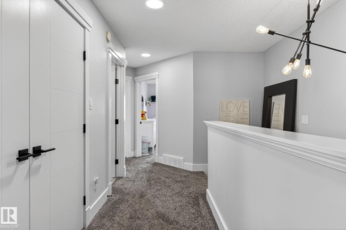 Carpeted hallway featuring contemporary white doors with black hardware, white baseboards, and a modern ceiling light fixture - 17733 64A Street, Edmonton, AB 