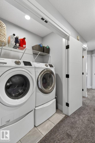 Dedicated laundry area with modern front-loading washer and dryer on pedestals, complemented by overhead wire shelving - 17733 64A Street, Edmonton, AB 