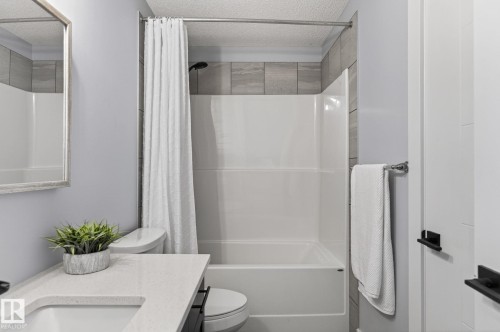 Bathroom featuring a tub/shower combination with light gray tile surround, light gray painted walls, and a white countertop vanity - 17733 64A Street, Edmonton, AB 