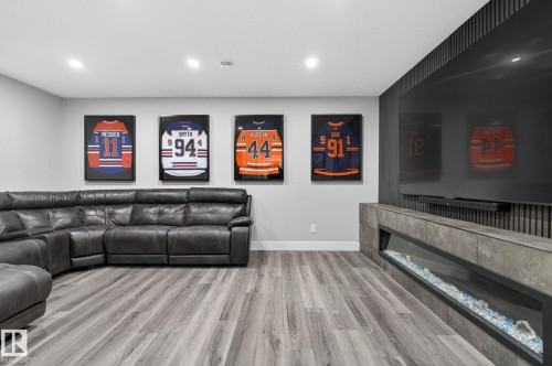 Recessed lighting illuminates wood-finish flooring and a contemporary fireplace featuring a linear glass-enclosed firebox set within a stone-look surround - 17733 64A Street, Edmonton, AB 