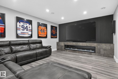 Media room featuring wood-finish flooring, recessed lighting, and a linear electric fireplace with a stone-finish surround - 17733 64A Street, Edmonton, AB 