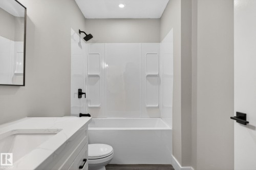 Bathroom featuring a white bathtub with a shower kit, matte black fixtures, a white vanity with an integrated sink, a matching countertop, and a dark wood-finish floor - 17733 64A Street, Edmonton, AB 