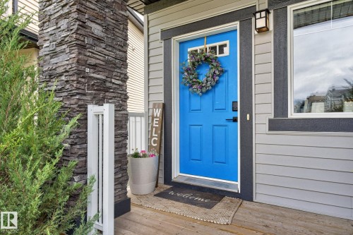 Vibrant blue entry door with a multi-pane transom window, flanked by gray siding and a stacked stone column - 17733 64A Street, Edmonton, AB 