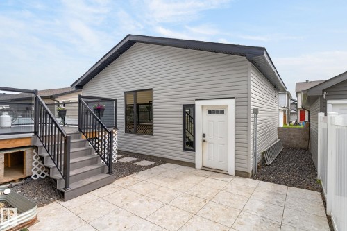 Rear exterior featuring light gray siding, a deck with black railings and glass panels, and a ground-level patio with large format pavers - 17733 64A Street, Edmonton, AB 