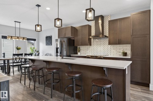 Kitchen featuring a large island with a light-toned countertop, stainless steel appliances, dark wood-finish cabinetry, a white herringbone subway tile backsplash, and wood-finish flooring - 17733 64A Street, Edmonton, AB 