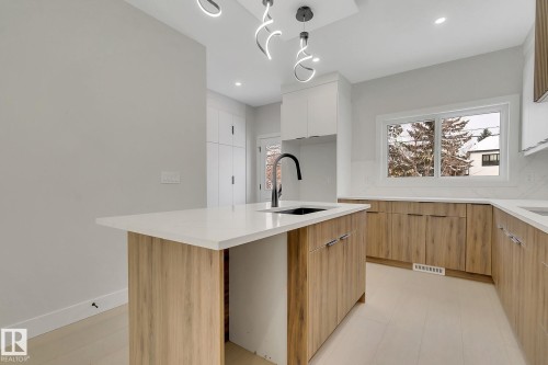 Modern kitchen with a central island featuring a white countertop and wood-finish cabinetry - 11132 72 Avenue, Edmonton, AB - Indoor Photo Showing Kitchen
