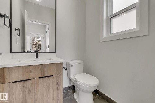 Bathroom featuring a wood-finish vanity with a white countertop, an undermount sink, and a black-framed mirror - 11132 72 Avenue, Edmonton, AB - Indoor Photo Showing Bathroom