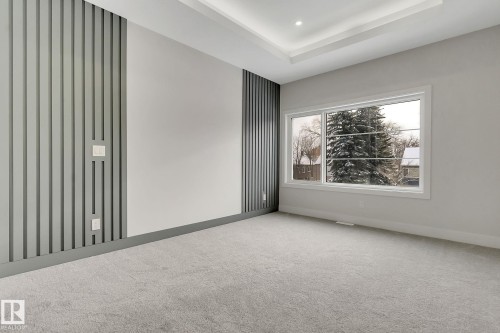Spacious room featuring a contemporary accent wall with vertical paneling, light gray carpeting, a large multipane window, and a tray ceiling with recessed lighting - 11132 72 Avenue, Edmonton, AB - Indoor Photo Showing Other Room
