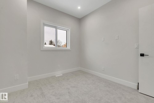 Spacious room featuring light gray carpeting, a bright window with white trim, and a contemporary white door with matte black hardware - 11132 72 Avenue, Edmonton, AB - Indoor Photo Showing Other Room