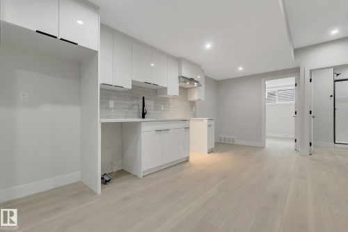 Contemporary kitchen area featuring white cabinetry, light wood-finish flooring, recessed lighting, a subway tile backsplash, and a black-finish faucet - 11132 72 Avenue, Edmonton, AB - Indoor
