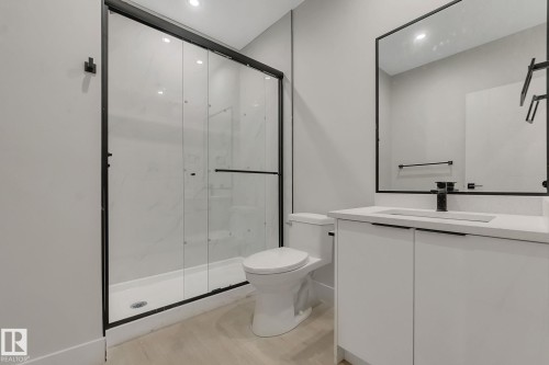 Contemporary bathroom featuring a glass-enclosed shower with black framing, a white vanity with integrated sink, a rectangular framed mirror, and light-toned flooring - 11132 72 Avenue, Edmonton, AB - Indoor Photo Showing Bathroom