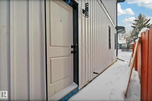 White paneled entry door with dark hardware, flanked by vertical siding and a modern exterior light fixture - 11132 72 Avenue, Edmonton, AB -  With Exterior