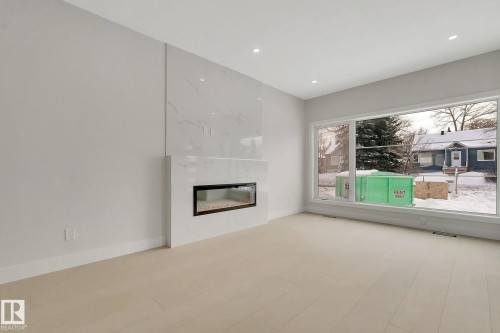 Spacious room featuring a contemporary fireplace with white surround, large picture windows, recessed lighting, light-toned wood-finish flooring, and crisp white baseboards - 11132 72 Avenue, Edmonton, AB - Indoor Photo Showing Living Room With Fireplace