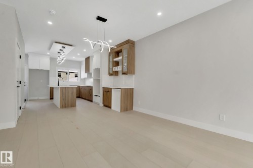 Contemporary kitchen with wood-finish flooring, a central island featuring a white countertop and dark faucet, a white tile backsplash, and two-tone cabinetry with glass-front uppers - 11132 72 Avenue, Edmonton, AB - Indoor Photo Showing Kitchen