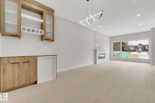 Contemporary open-concept interior featuring light wood-finish flooring, a built-in wet bar with wood-finish cabinetry, a modern fireplace with a tiled surround, a large picture window, and recessed lighting - 11132 72 Avenue, Edmonton, AB - Indoor Photo Showing Other Room