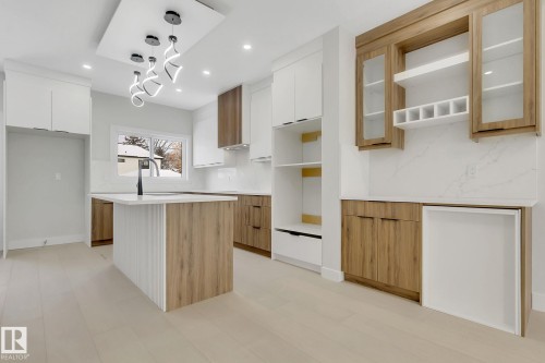 Spacious kitchen featuring a central island with integrated sink, two-tone cabinetry, light-toned wood-finish flooring, white countertops, and contemporary ceiling lighting - 11132 72 Avenue, Edmonton, AB - Indoor Photo Showing Kitchen