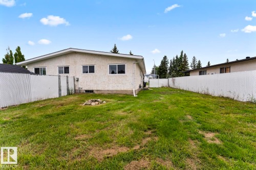 Expansive grassy yard with a white chain-link fence, mature trees, and a stucco exterior - 210 22 Street, Cold Lake, AB 