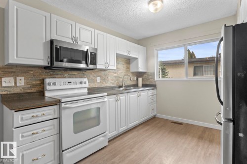 Kitchen featuring white shaker-style cabinetry, a stainless steel microwave, a white electric range, wood-finish flooring, and a large window - 210 22 Street, Cold Lake, AB 