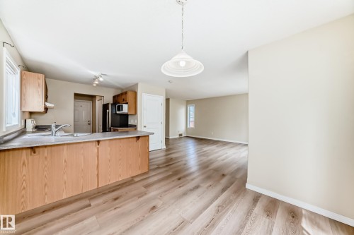 Open-concept kitchen and living area featuring wood-finish flooring, light wood cabinetry, a light-toned countertop, and a double-basin sink - 3711 22A St, Edmonton, AB 