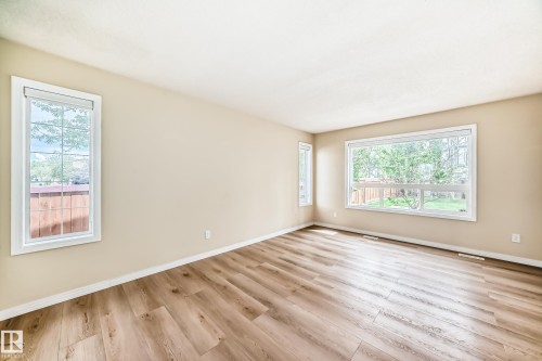Spacious room featuring wood-finish flooring, light-toned walls, multiple large windows with white trim, and white baseboards - 3711 22A St, Edmonton, AB 