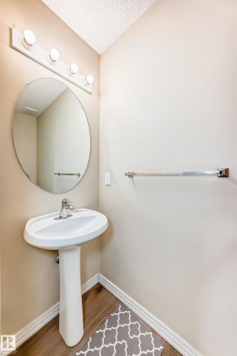 Pedestal sink with chrome faucet, complemented by a circular mirror and a four-bulb vanity light fixture - 3711 22A St, Edmonton, AB 