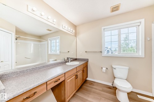 Spacious bathroom featuring a wood-finish vanity with a single basin sink, a large wall-mounted mirror, and a built-in shower-tub combination - 3711 22A St, Edmonton, AB 