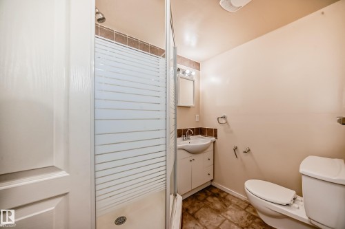 Full bathroom featuring a shower stall with a patterned glass enclosure, a white ceramic toilet, and a vanity with an integrated sink - 3711 22A St, Edmonton, AB 