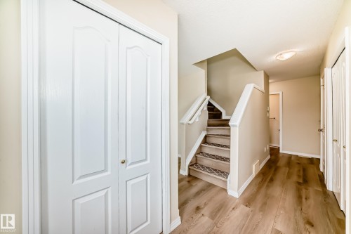 Foyer featuring wood-finish flooring, white bi-fold closet doors, and a staircase with patterned risers and white railings - 3711 22A St, Edmonton, AB 