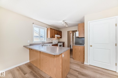 Kitchen featuring wood-finish flooring, light wood cabinetry, laminate countertops, a stainless steel sink, and white appliances - 3711 22A St, Edmonton, AB 