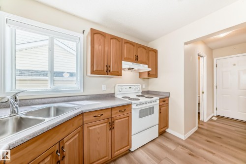 Kitchen featuring wood cabinetry, a double basin stainless steel sink with a chrome faucet, a white electric range, and light-toned countertops - 3711 22A St, Edmonton, AB 