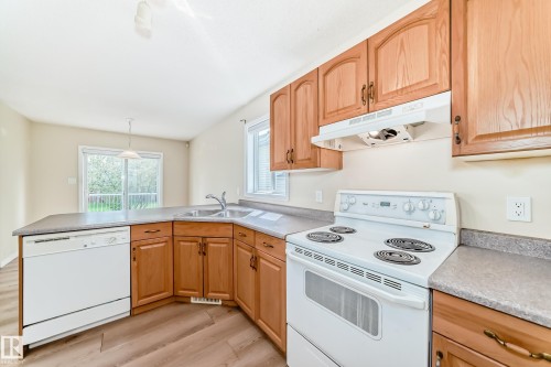 Kitchen featuring wood-finish cabinetry, a white electric range, a double basin stainless steel sink, and wood-finish flooring - 3711 22A St, Edmonton, AB 