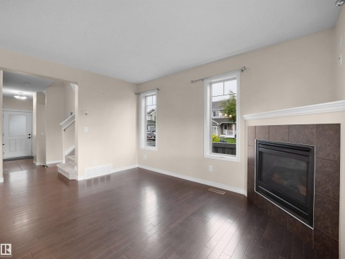 Living area featuring wood-finish flooring, a fireplace with a tiled surround and white mantel, and two large windows - 21316 45A Avenue Nw, Edmonton, AB 