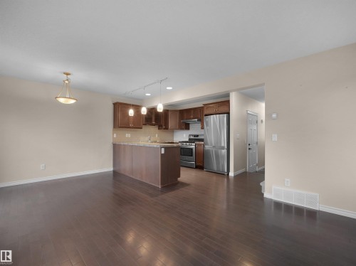 Open-concept living space featuring wood-finish flooring, a kitchen island with seating, stainless steel appliances, dark wood cabinetry, and recessed lighting - 21316 45A Avenue Nw, Edmonton, AB 