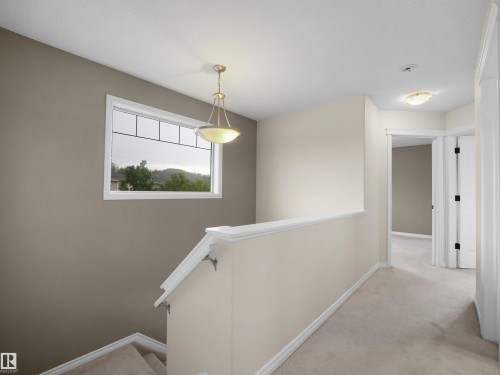 Carpeted upper hallway featuring a window with grid detailing, a pendant light fixture, and a built-in stair railing - 21316 45A Avenue Nw, Edmonton, AB 