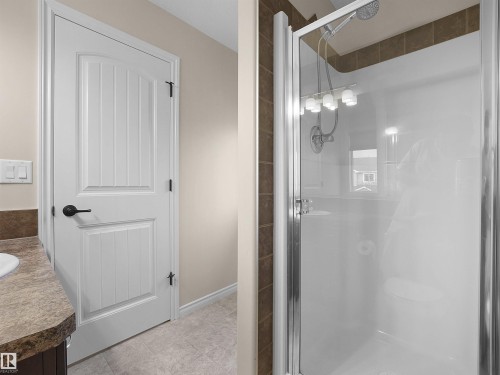 Bathroom featuring a white paneled door, a shower with a clear glass enclosure, and a vanity with a stone-finish countertop - 21316 45A Avenue Nw, Edmonton, AB 