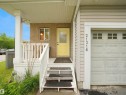 Entryway featuring a bright yellow door, brick and siding exterior, white railing, and an attached garage with panel detailing - 21316 45A Avenue Nw, Edmonton, AB 