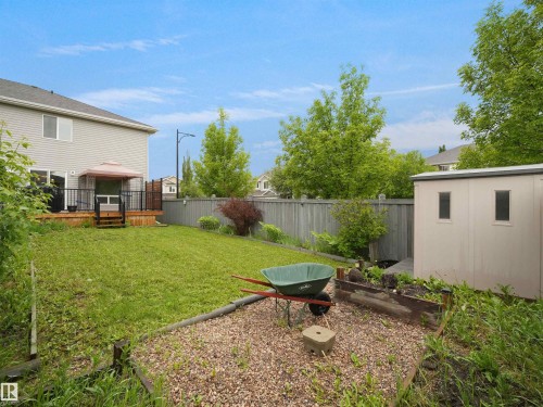 Expansive backyard featuring a spacious wood-decked patio with black railings, a manicured lawn, an outdoor storage shed, and a raised garden bed - 21316 45A Avenue Nw, Edmonton, AB 