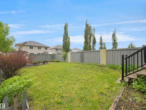 Expansive backyard featuring a green lawn, wood fencing, mature trees, a small garden bed, and a wood deck with black metal railings - 21316 45A Avenue Nw, Edmonton, AB 