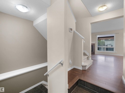 Multi-level interior featuring wood-finish flooring, a tiled entry, carpeted stairs with white railings, and neutral wall tones - 21316 45A Avenue Nw, Edmonton, AB 
