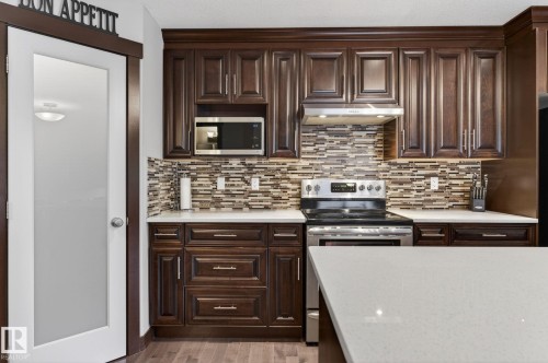 Kitchen featuring dark wood cabinetry with crown molding, stainless steel appliances, a mosaic tile backsplash, white countertops, and wood-finish flooring - 8506 80 Avenue, Edmonton, AB 