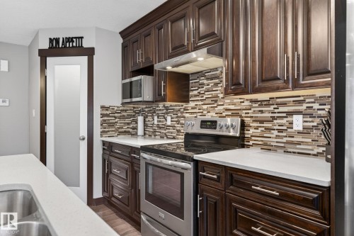 Kitchen featuring dark wood-finish cabinetry, light-toned countertops, and a full tile backsplash - 8506 80 Avenue, Edmonton, AB 