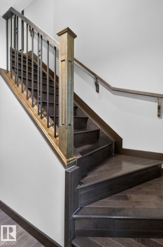 Hardwood staircase featuring dark wood-finish treads and risers, a light wood-finish newel post, black metal balusters, and a matching wood-finish handrail - 8506 80 Avenue, Edmonton, AB 